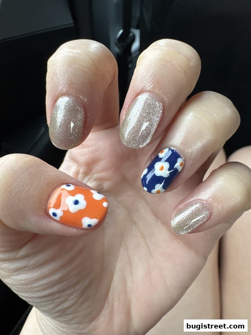 A close-up of a hand with beautifully manicured nails featuring a mix of glitter and floral designs.