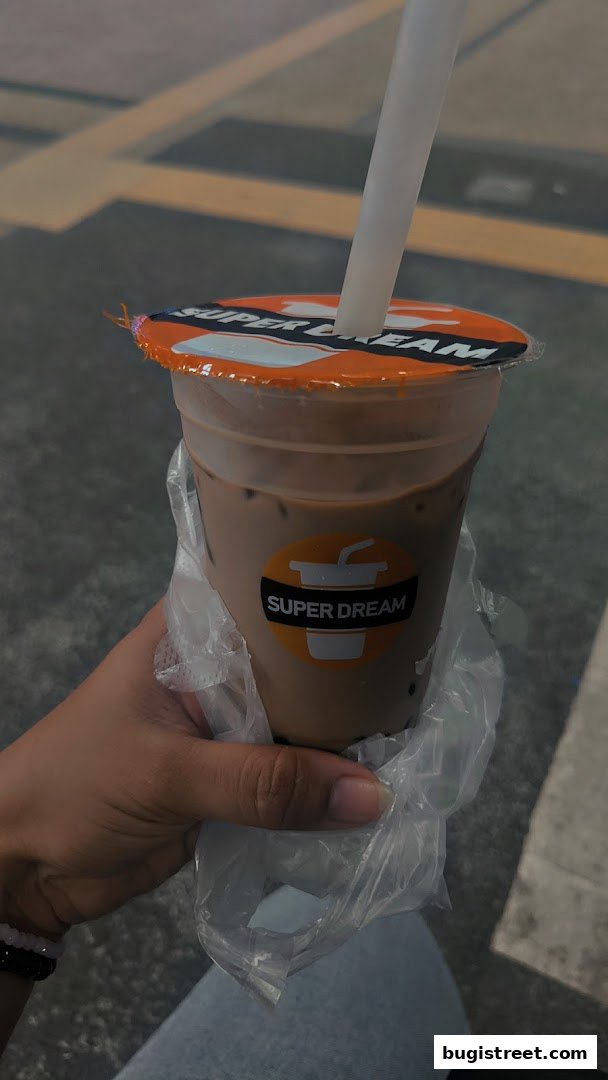 A hand holds a Super Dream branded beverage with a straw and plastic bag.