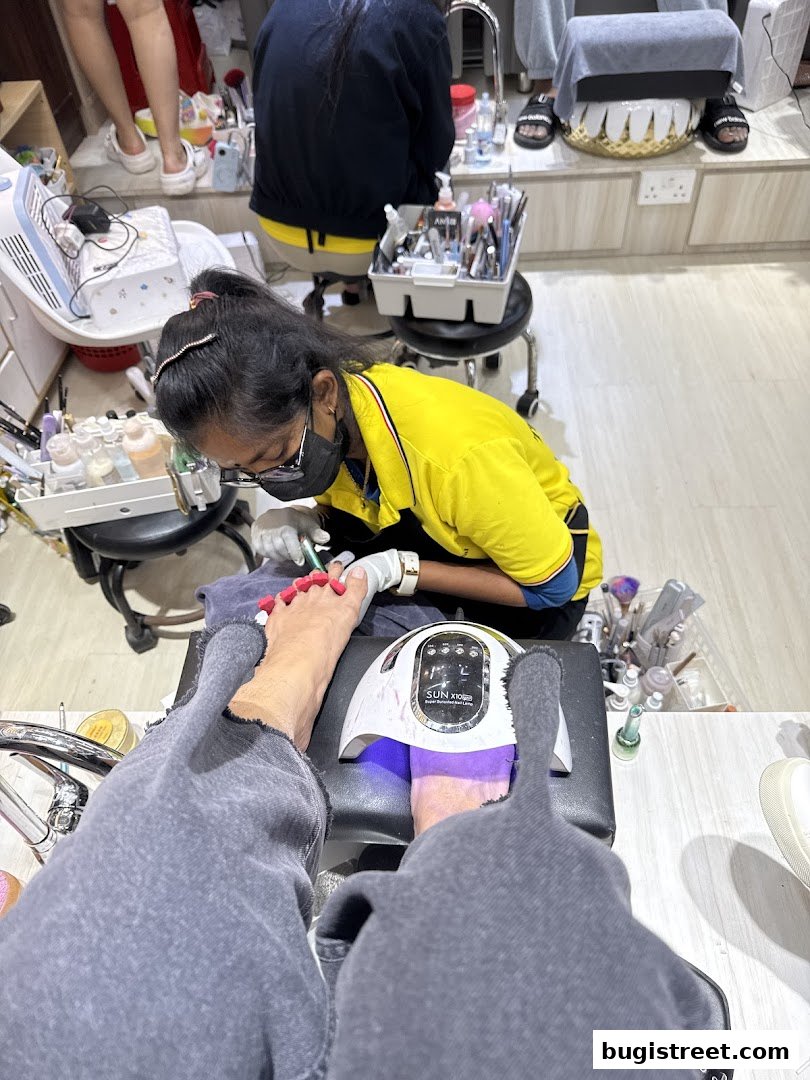 A nail technician is applying polish to a client's toes under a UV lamp.