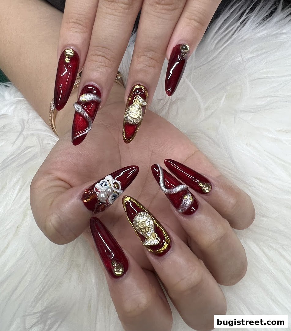 Close-up of hands with elaborate, long, dark red nails adorned with gold accents and 3D designs.
