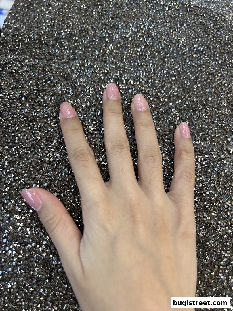 A hand with perfectly manicured, light pink nails against a sparkling, dark background.