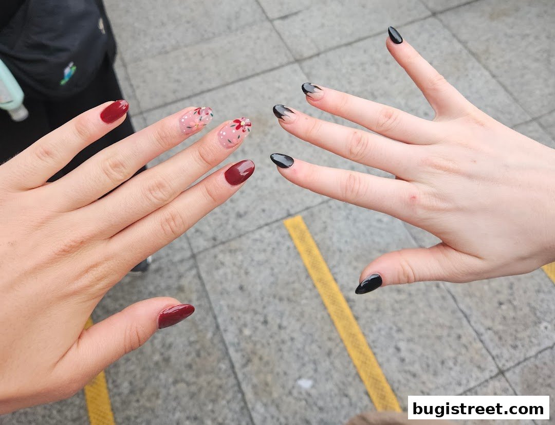 Two hands displaying different nail art styles, one with floral designs and the other with black French tips.