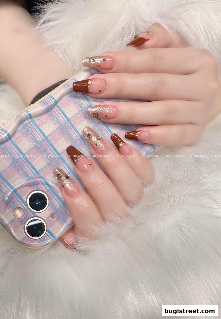 Close-up of hands with elegant brown and glittery nails, holding a phone.