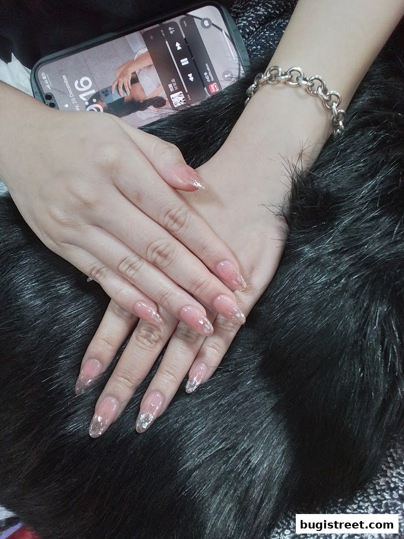 Close-up of hands with elegant, clear acrylic nails adorned with glitter.