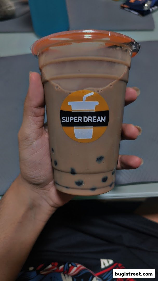 A hand holds a cup of bubble tea with the Super Dream logo.