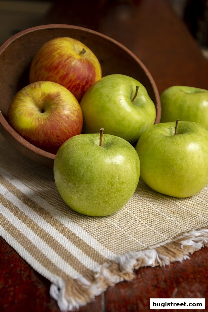 A rustic wooden bowl overflowing with fresh green and red apples on a striped cloth.