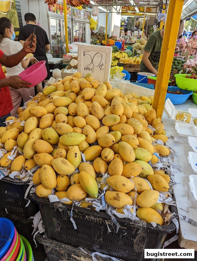 A large pile of fresh yellow mangoes displayed in black crates at a fruit stall.