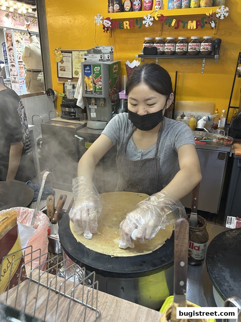 A person making a crepe with Nutella and other ingredients visible.