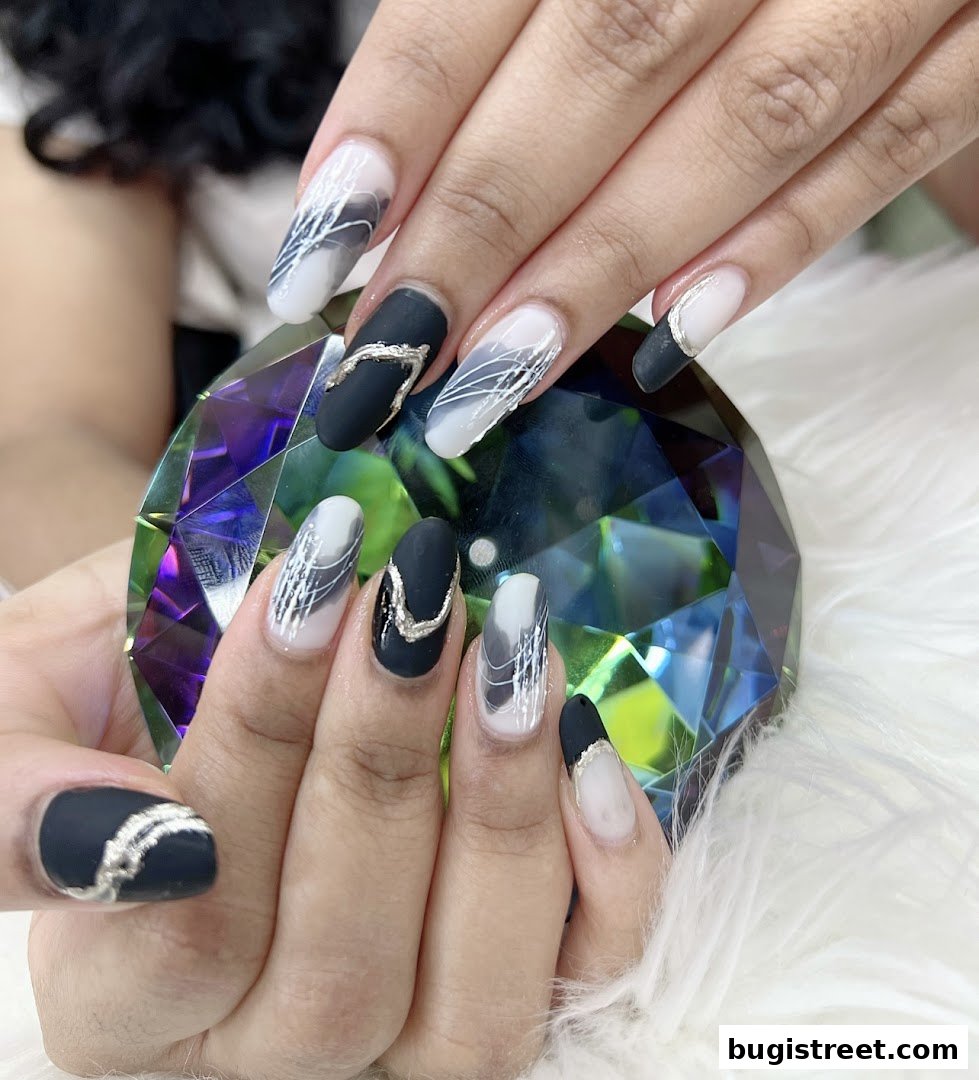 Close-up of hands with stylish black, white, and silver abstract nail art.