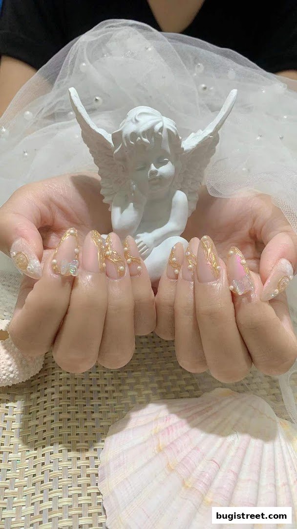 Close-up of hands with elaborate nail art featuring pearls and gold accents, with an angel figurine.