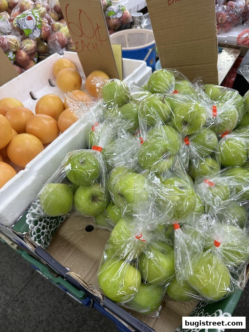 Fresh green apples and oranges displayed in boxes at a fruit stall.