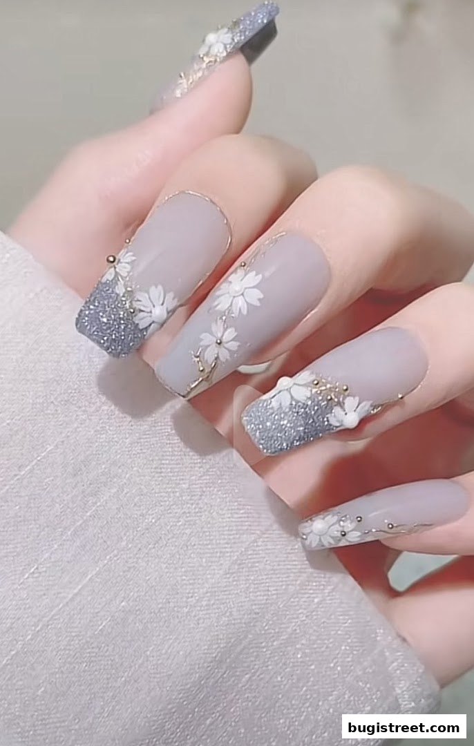Close-up of a hand with long, elegant nails featuring a delicate floral design and glitter accents.