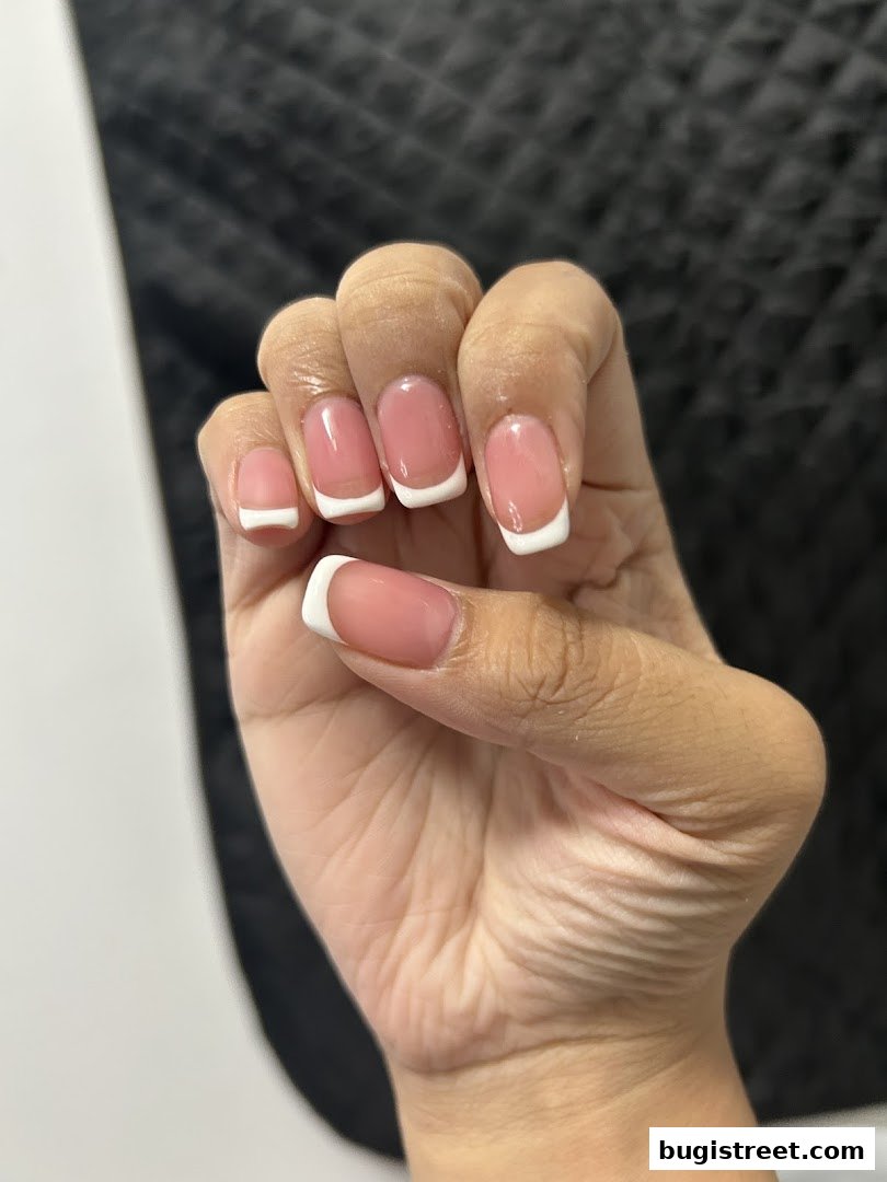 A close-up of a hand displaying perfectly manicured French tip nails.
