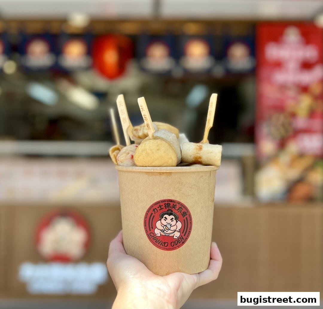 A hand holds a cup of Oden, a Japanese hot pot dish, with a sumo wrestler logo.