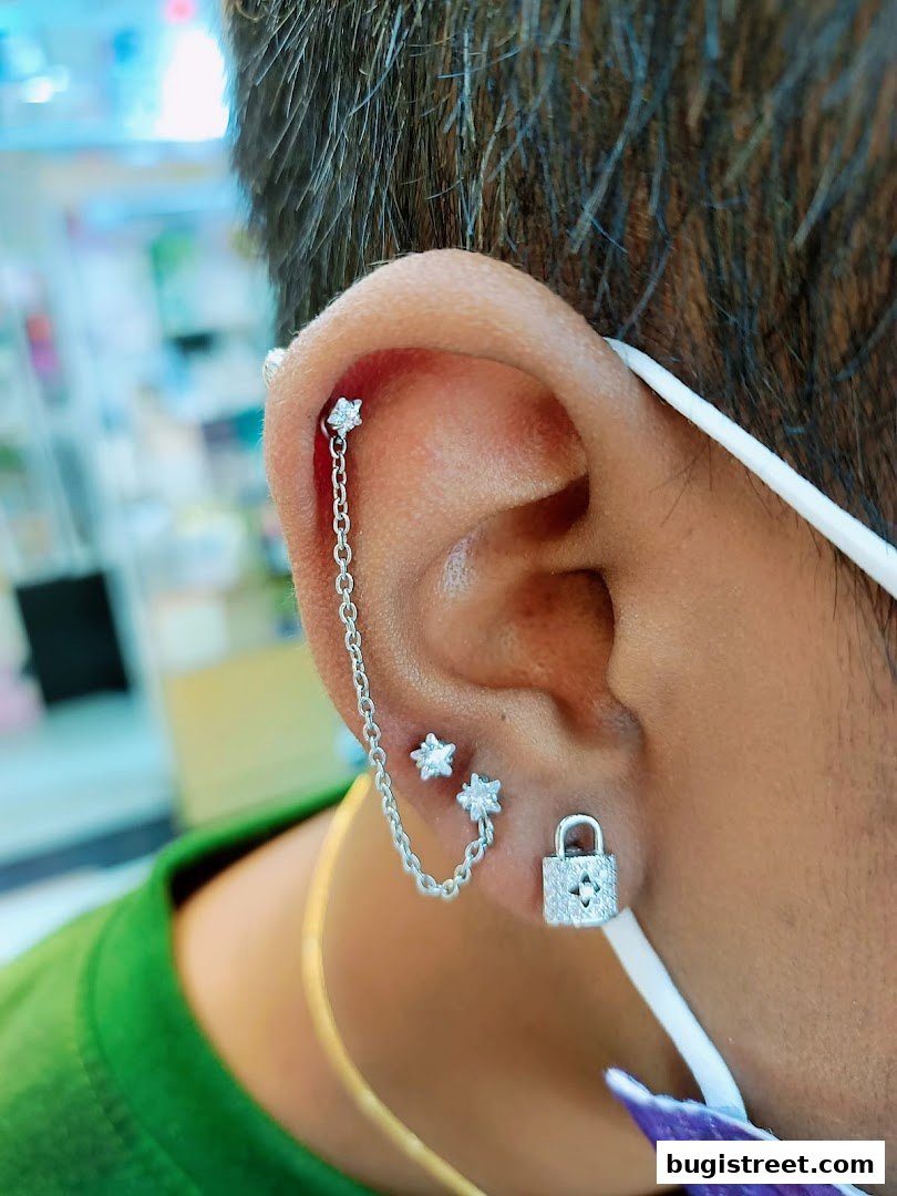 Close-up of an ear adorned with multiple sparkling piercings, including a chain and star-shaped studs.