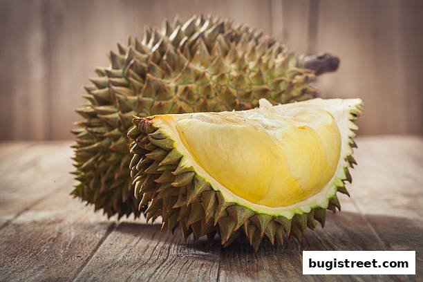 A whole durian and a cut piece of durian with its creamy flesh exposed.