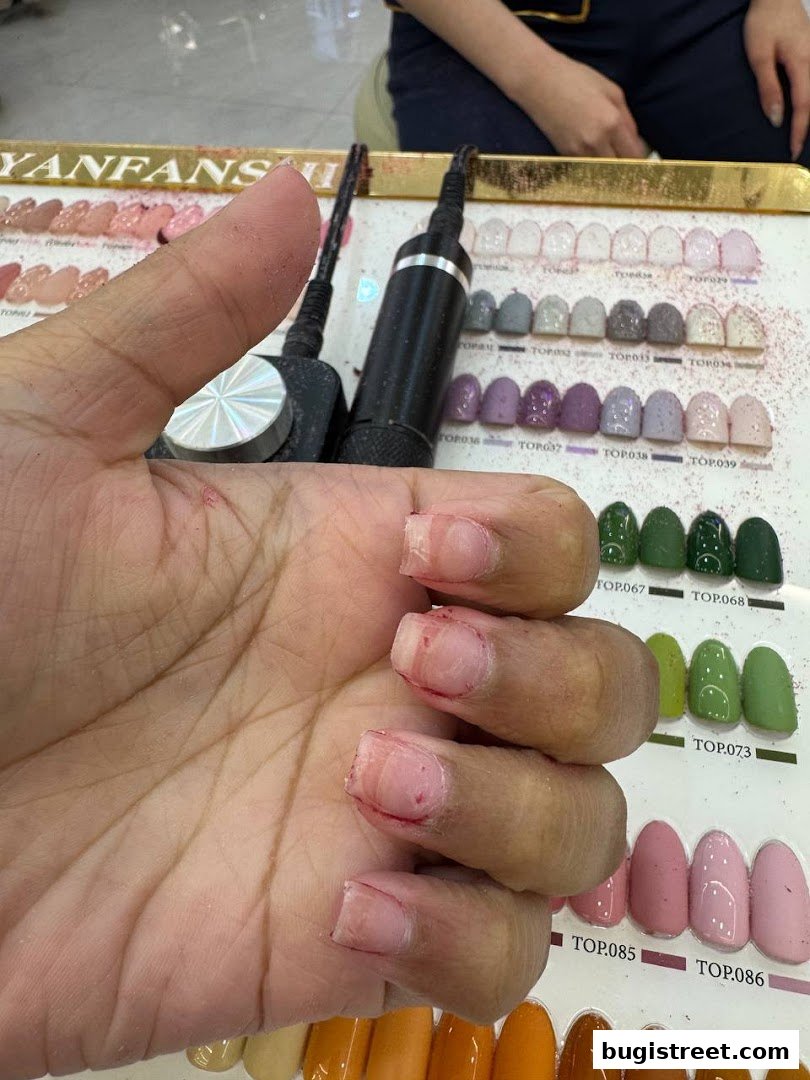 A hand with unpolished nails is shown next to a display of nail polish colors.