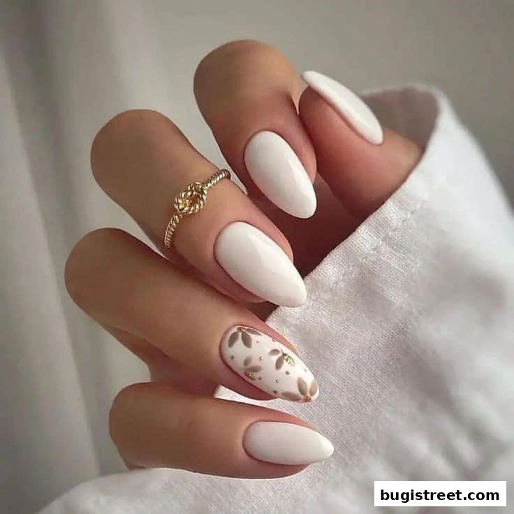A close-up of a hand with elegant white almond-shaped nails, one accented with a floral design.