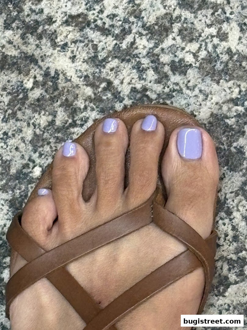 A close-up of a foot with lavender-colored toenails and brown sandals.