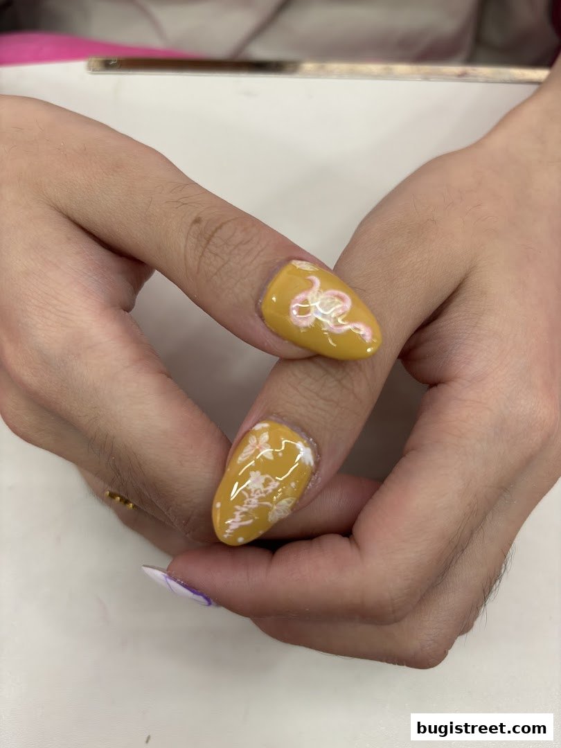 Close-up of hands with intricately designed yellow nails featuring snake and floral patterns.