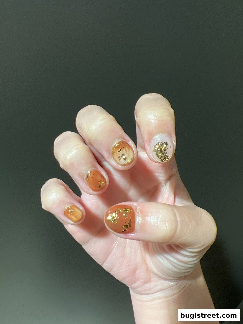 A hand with beautifully designed nails featuring a mix of warm brown and gold glitter.
