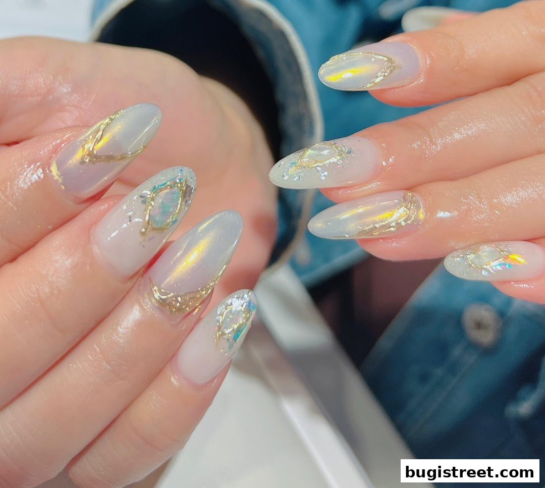 Close-up of hands with elegant, pearlescent oval nails adorned with gold accents and iridescent gems.