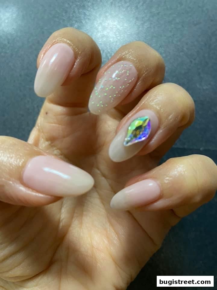 A close-up of a hand with beautifully manicured nails featuring a subtle glitter and a striking rhinestone.