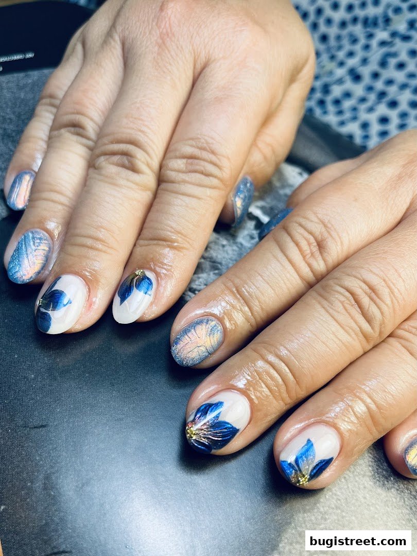 Close-up of hands with intricate blue floral nail art and shimmering accents.
