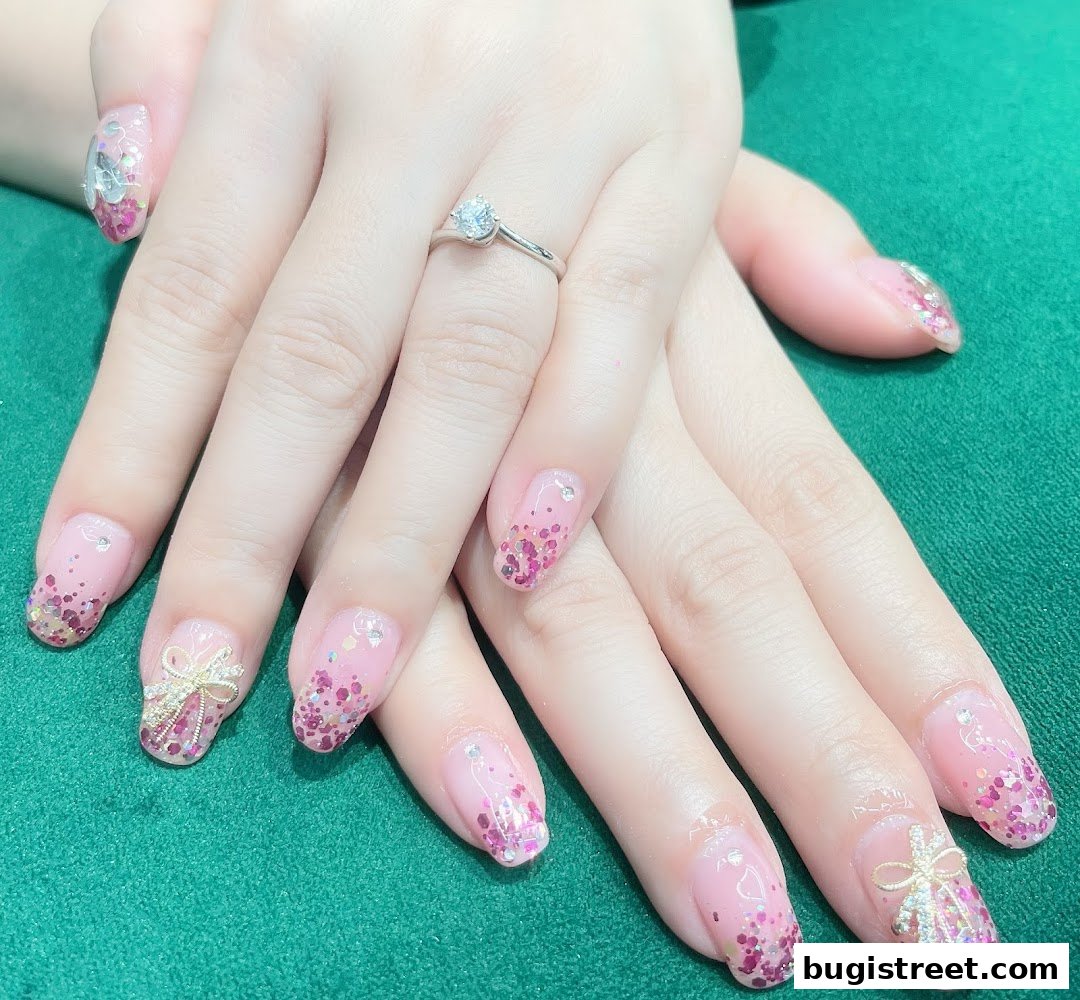 Close-up of hands with beautifully decorated pink and glittery nails, featuring a diamond ring.