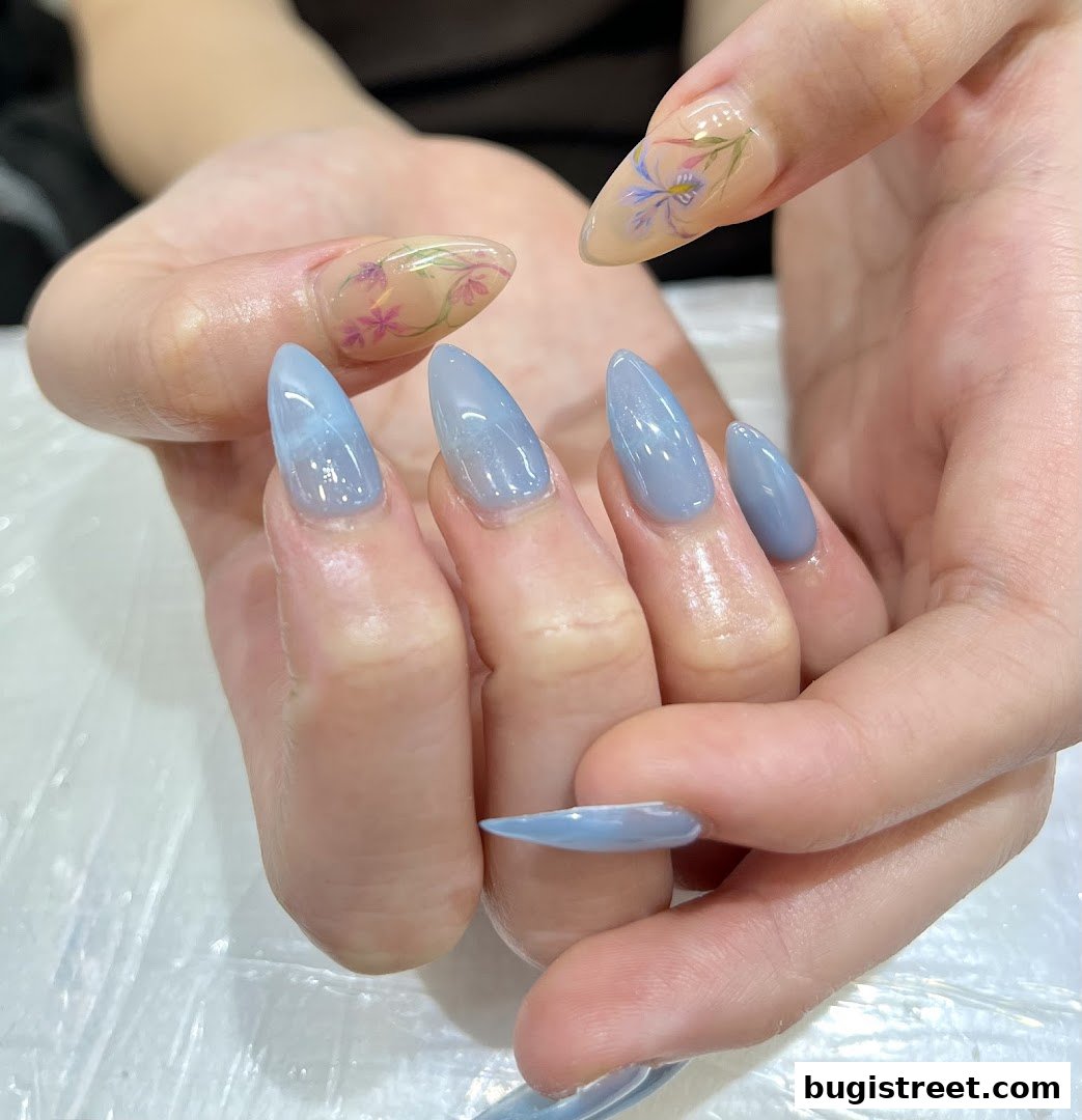 Close-up of hands with beautifully designed stiletto nails in blue and floral patterns.