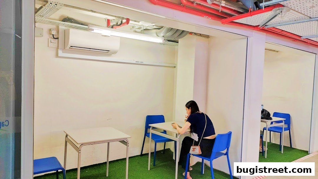 A woman sits at a table in a minimalist cafe with blue chairs and artificial grass flooring.