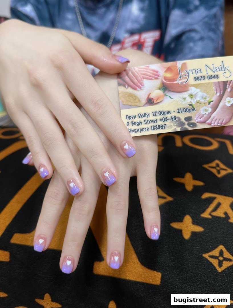 A person displays beautifully manicured nails with a purple gradient and heart design.