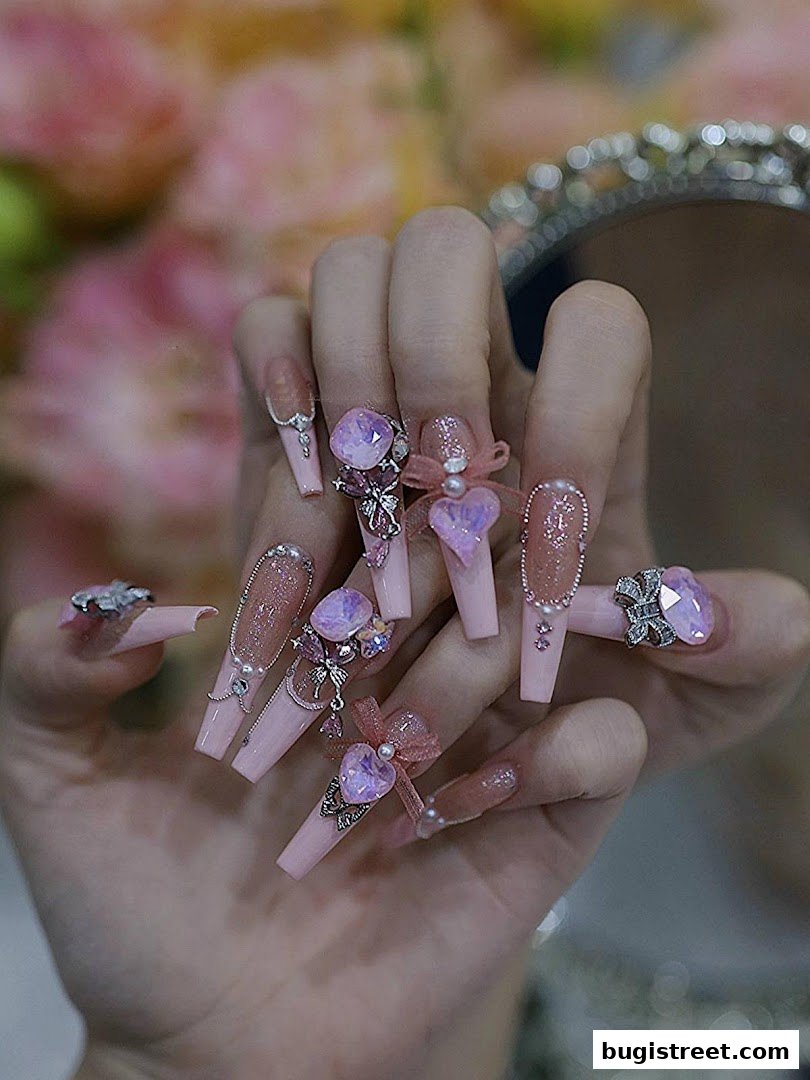 Close-up of hands with elaborately decorated pink coffin-shaped nails adorned with gems and bows.
