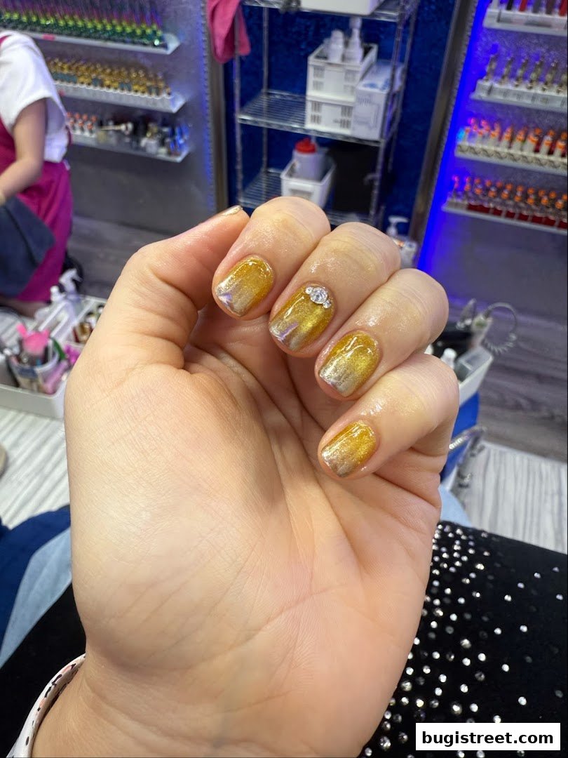 A close-up of a hand with beautifully designed golden ombre nails adorned with rhinestones.