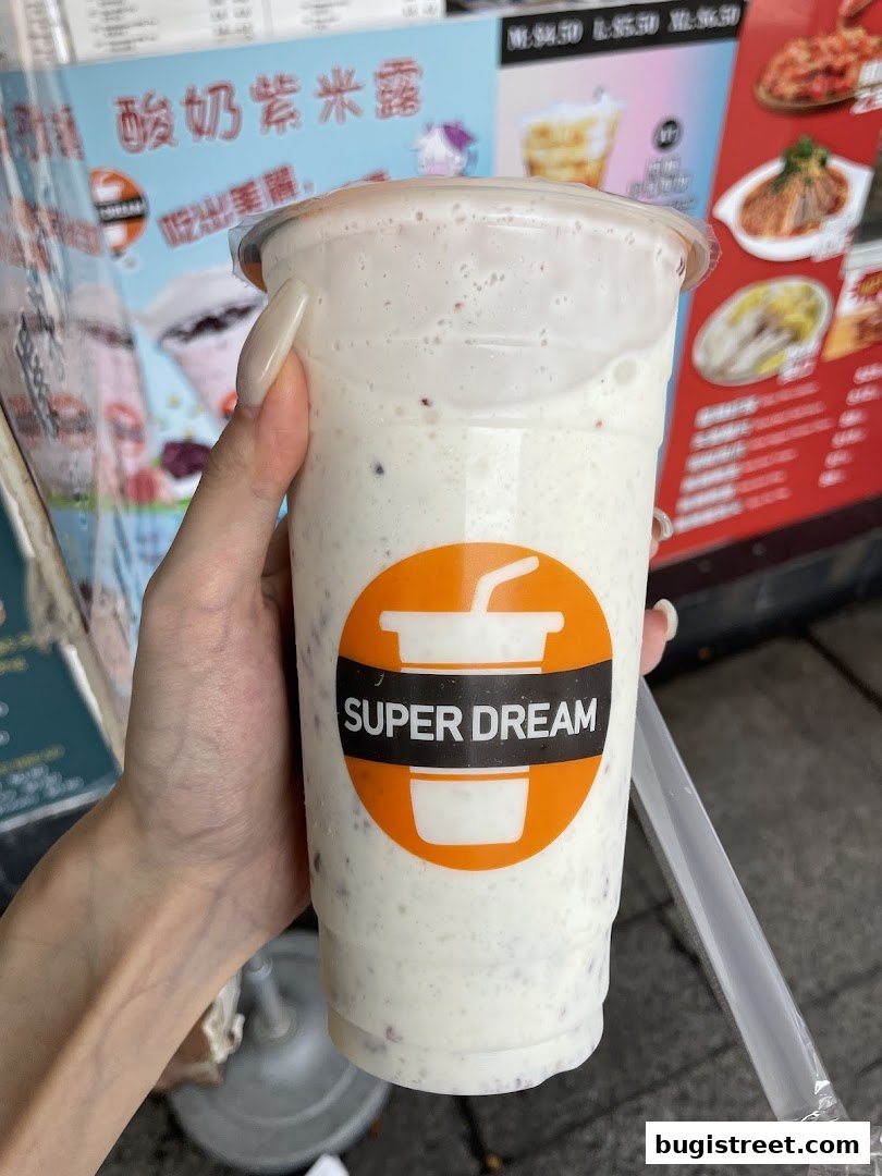 A hand holds a creamy beverage with the Super Dream logo against a backdrop of menu boards.