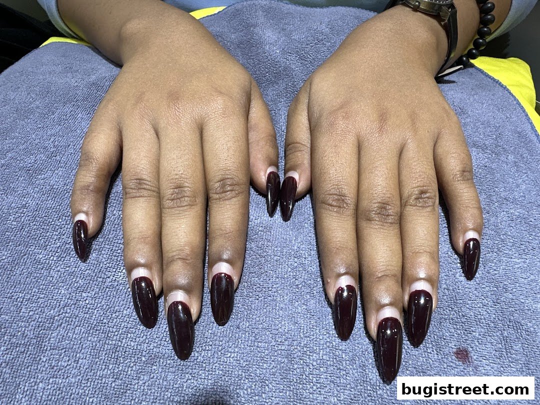 A close-up of hands with perfectly manicured, dark red stiletto nails.