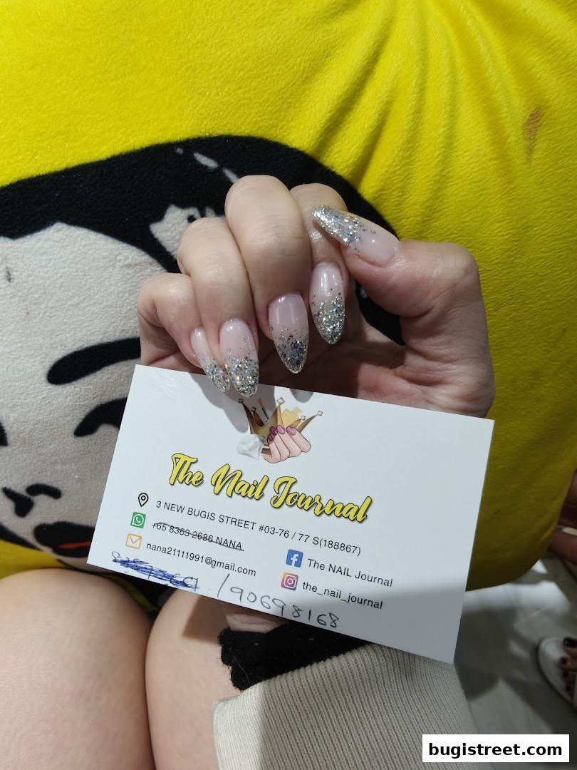 A person displays their beautifully manicured nails holding a business card for 'The Nail Journal'.