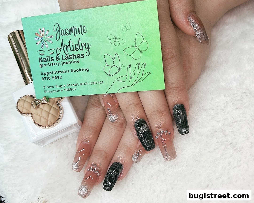 A close-up of beautifully designed nails with a business card and nail polish bottle.