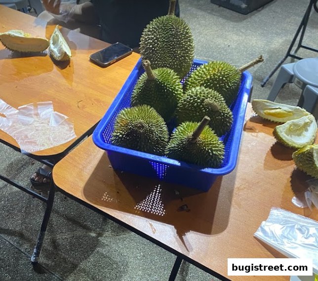 A basket of fresh durians and opened durian pieces on a wooden table.