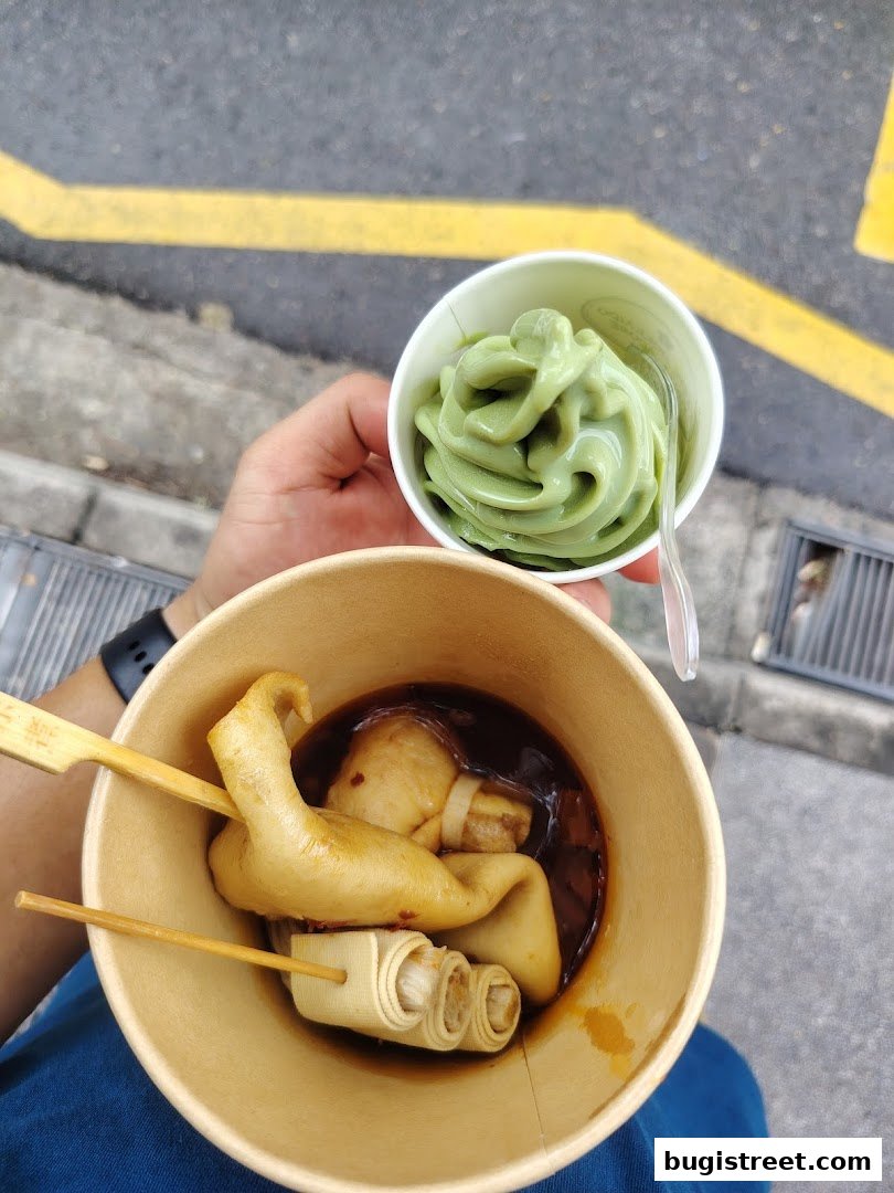 A person holds a cup of green soft serve ice cream and a bowl of oden.