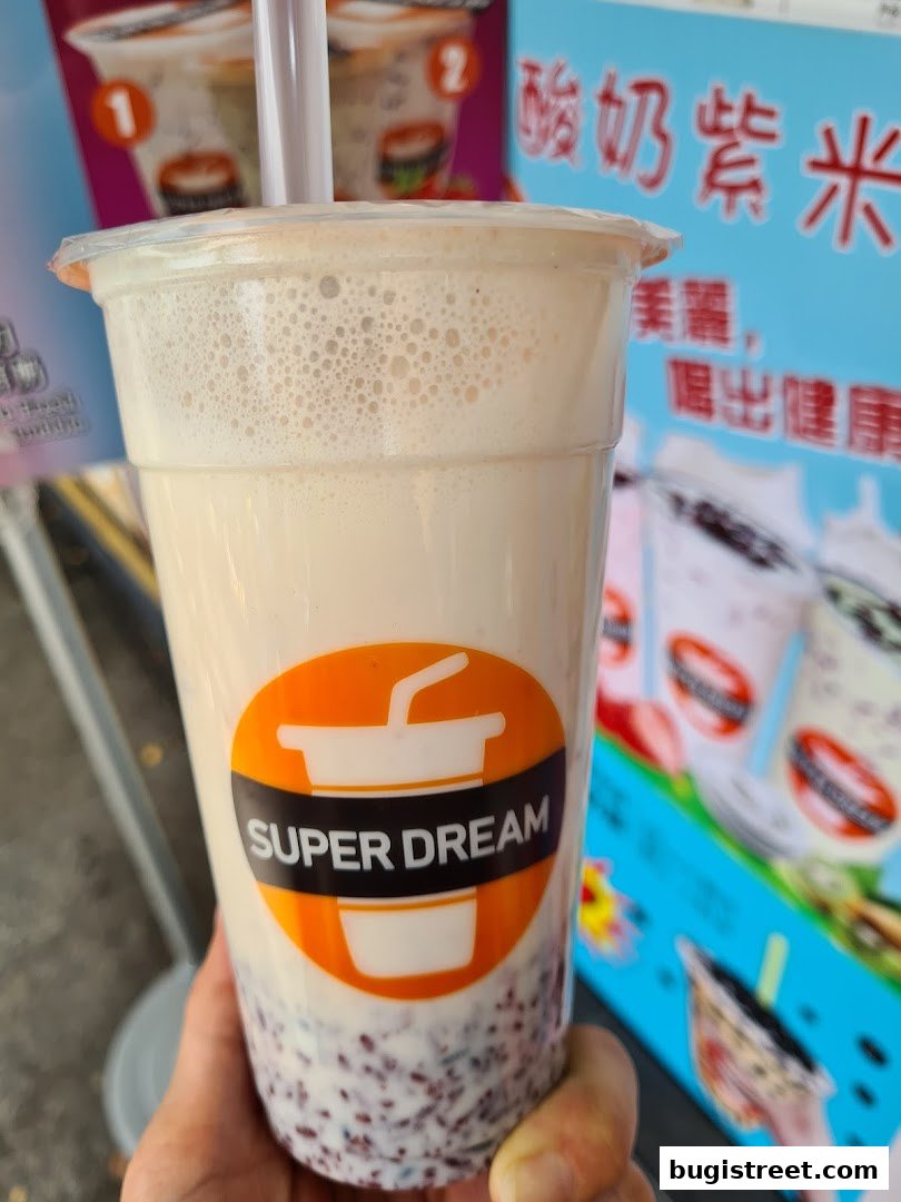 A hand holds a cup of Super Dream beverage with purple rice at the bottom.