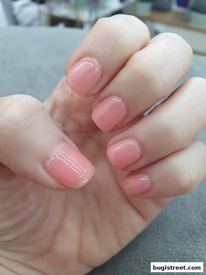 A close-up of a hand with perfectly manicured, glossy, light pink gel nails.