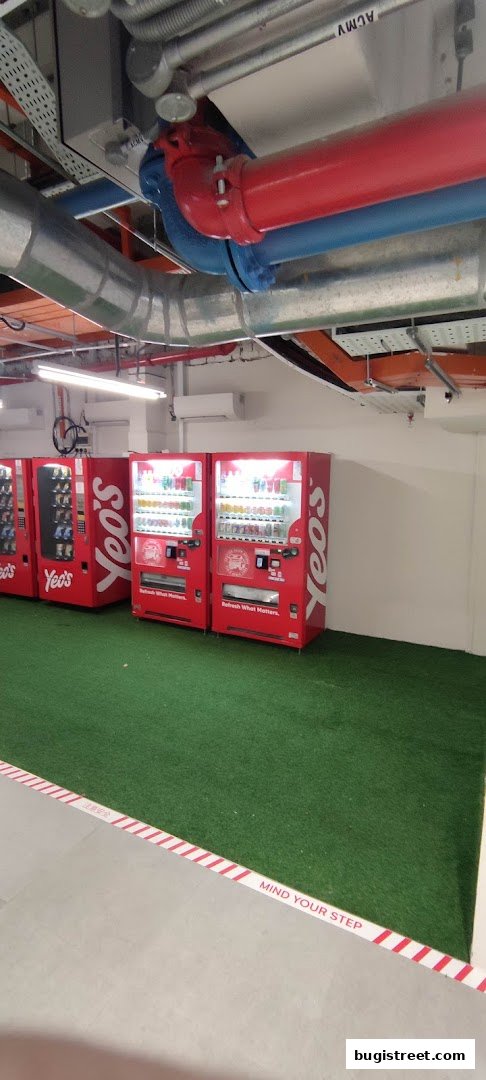Red Yeo's vending machines lined up on a green carpeted area with overhead pipes.