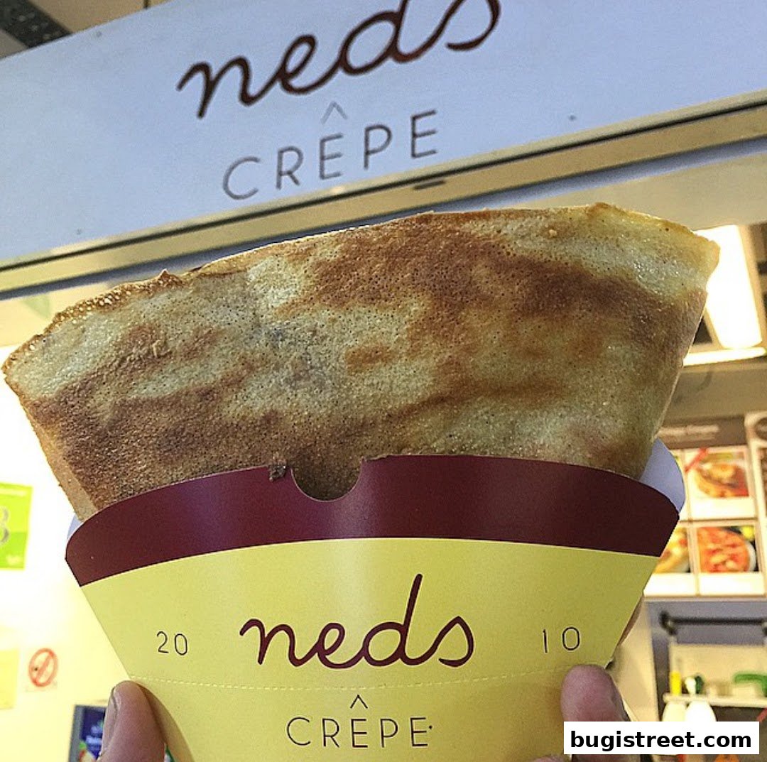 A person holds a freshly made crepe from Neds Crepe, with the shop's logo visible.