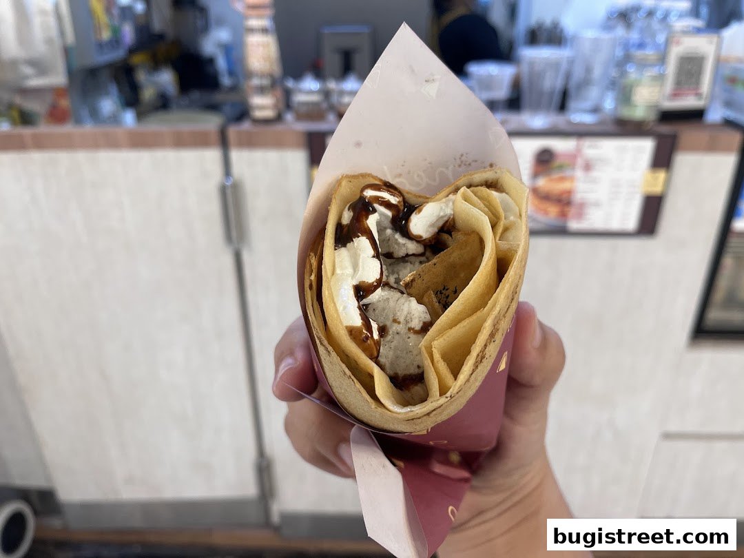 A hand holds a delicious crepe filled with cream and chocolate sauce.