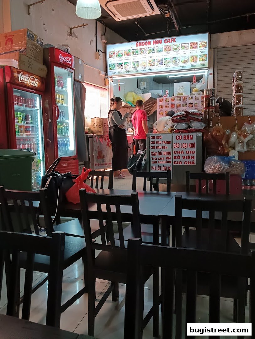 Interior of Shoon Kou Cafe with seating, menu board, and staff preparing food.