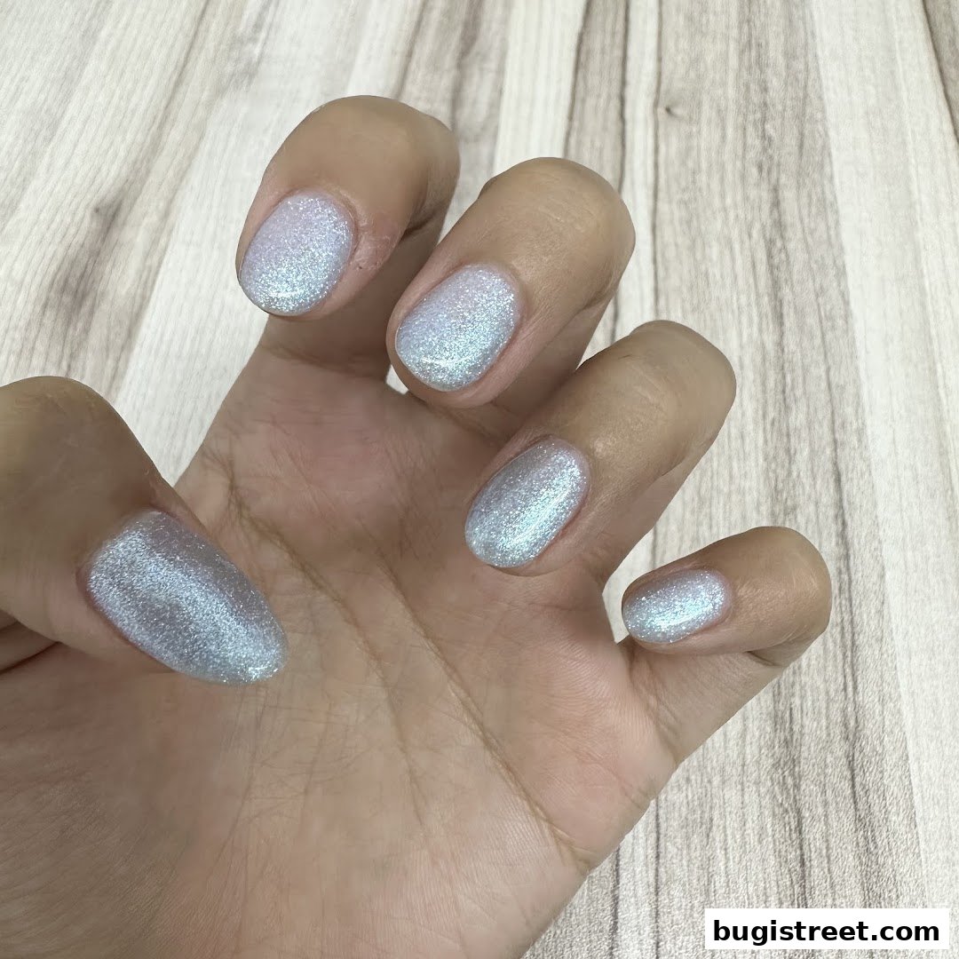 A hand with perfectly manicured nails painted in a shimmering, light blue glitter polish.