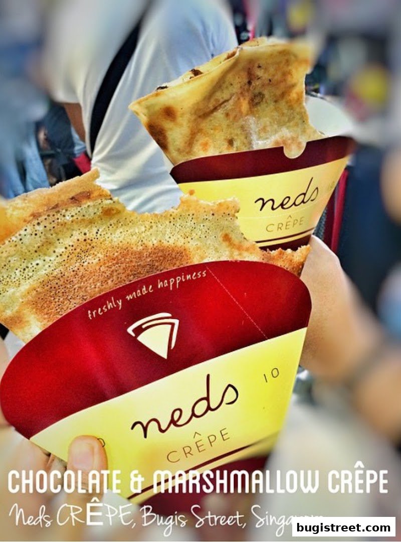 Close-up of two chocolate and marshmallow crepes being held, with the shop's branding visible.