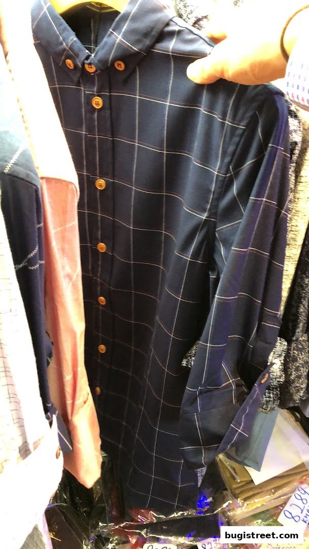 A person holds up a navy blue checkered shirt with gold buttons.