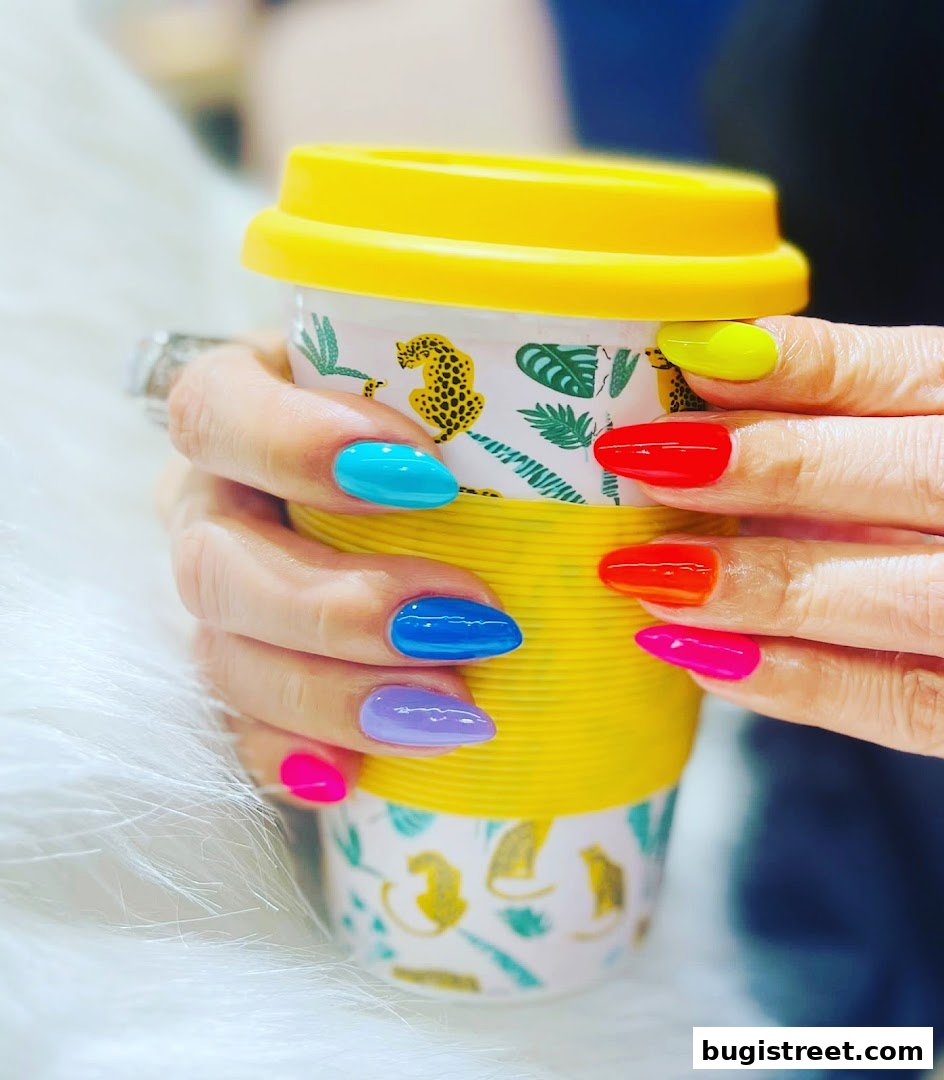 Hands with vibrant, multi-colored nails holding a decorative cup.